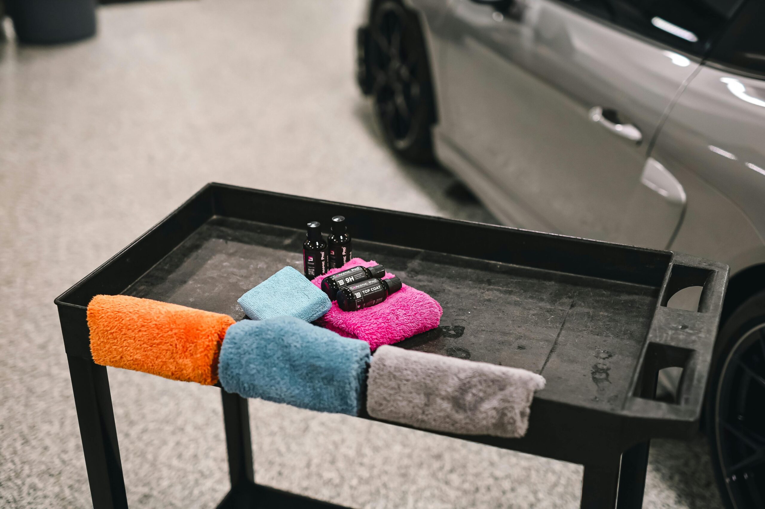 Colorful towels and detailing products on a cart beside a car in a garage.